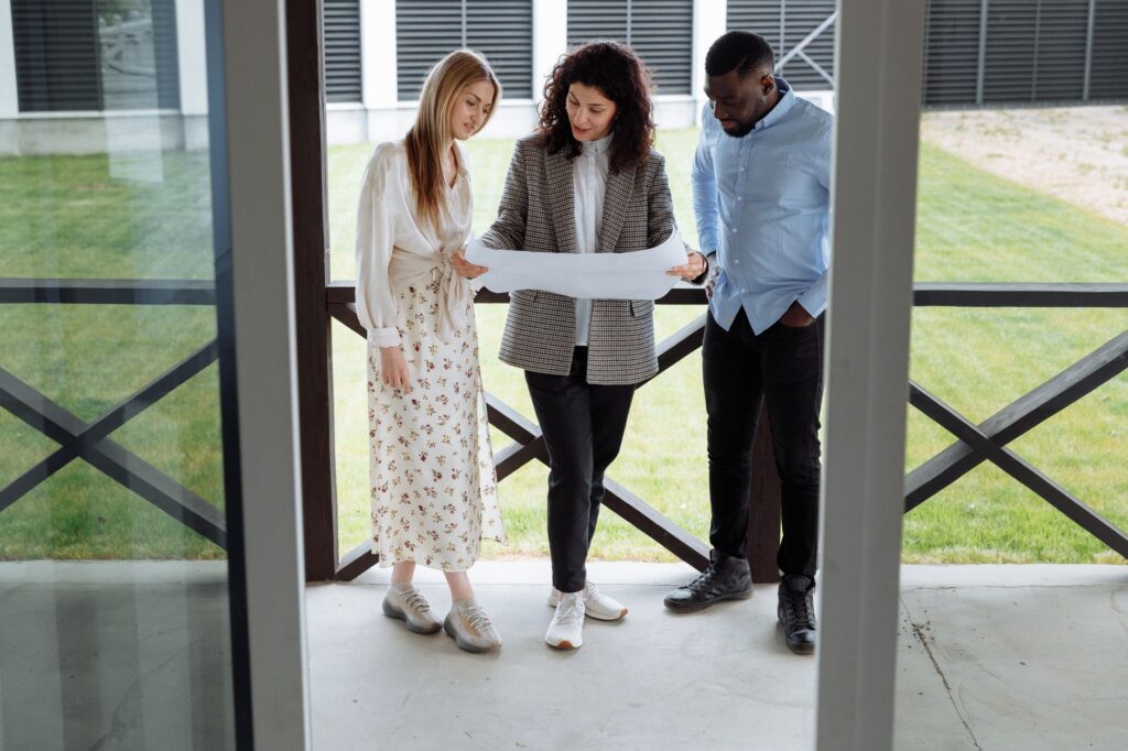 A realtor with clients examining a floor plan outside a modern property.