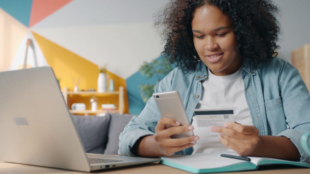 Young woman shopping online using smartphone and credit card at home.