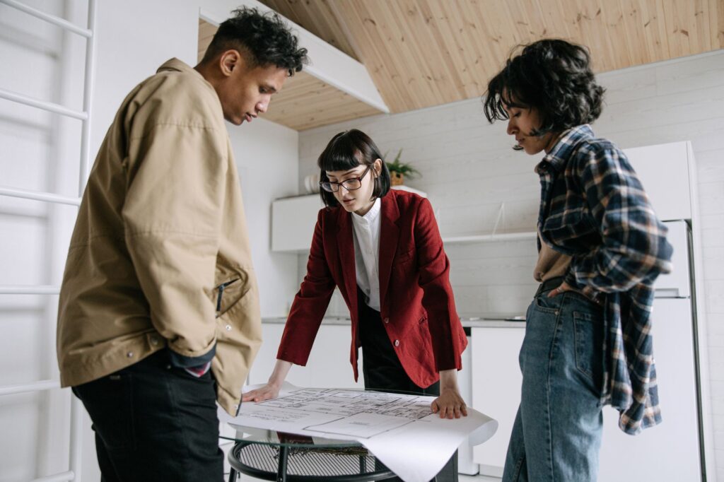 A real estate agent discusses property plans with a young couple indoors.