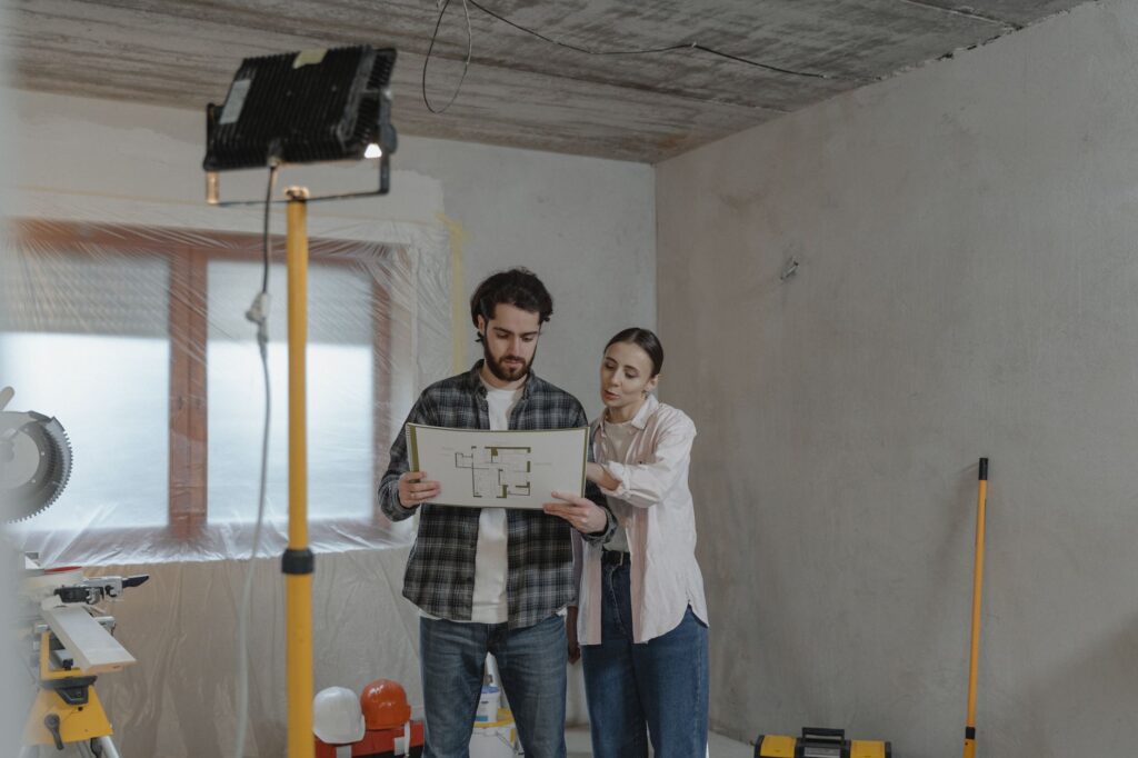 A couple examines blueprints in a partially renovated room, planning home improvements.
